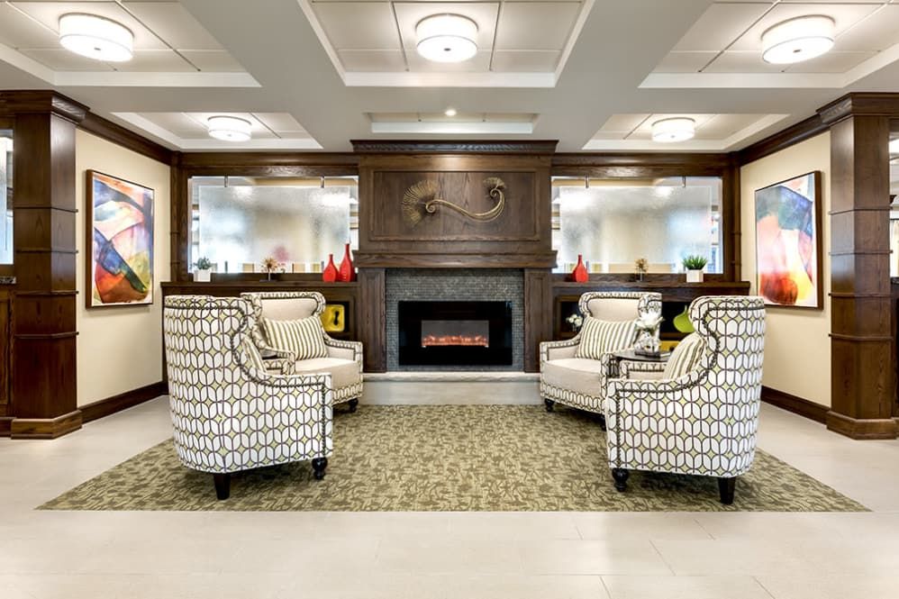 A cozy and elegant living room with patterned chairs arranged around a fireplace, complemented by wood paneling and elegant lighting.