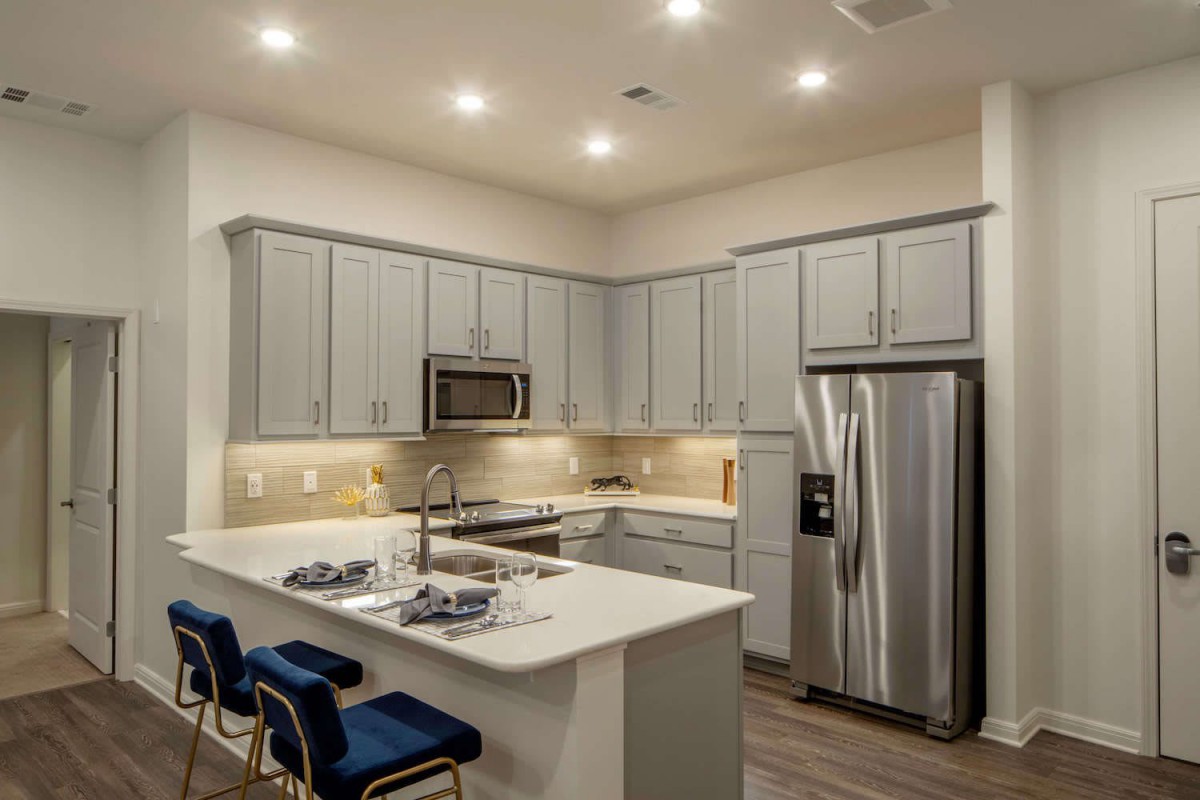 A modern kitchen with gray cabinets, stainless steel appliances, and a central island with bar stools.