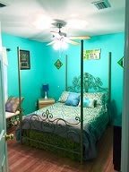 A cozy bedroom with turquoise walls, featuring a four-poster bed and ceiling fan.