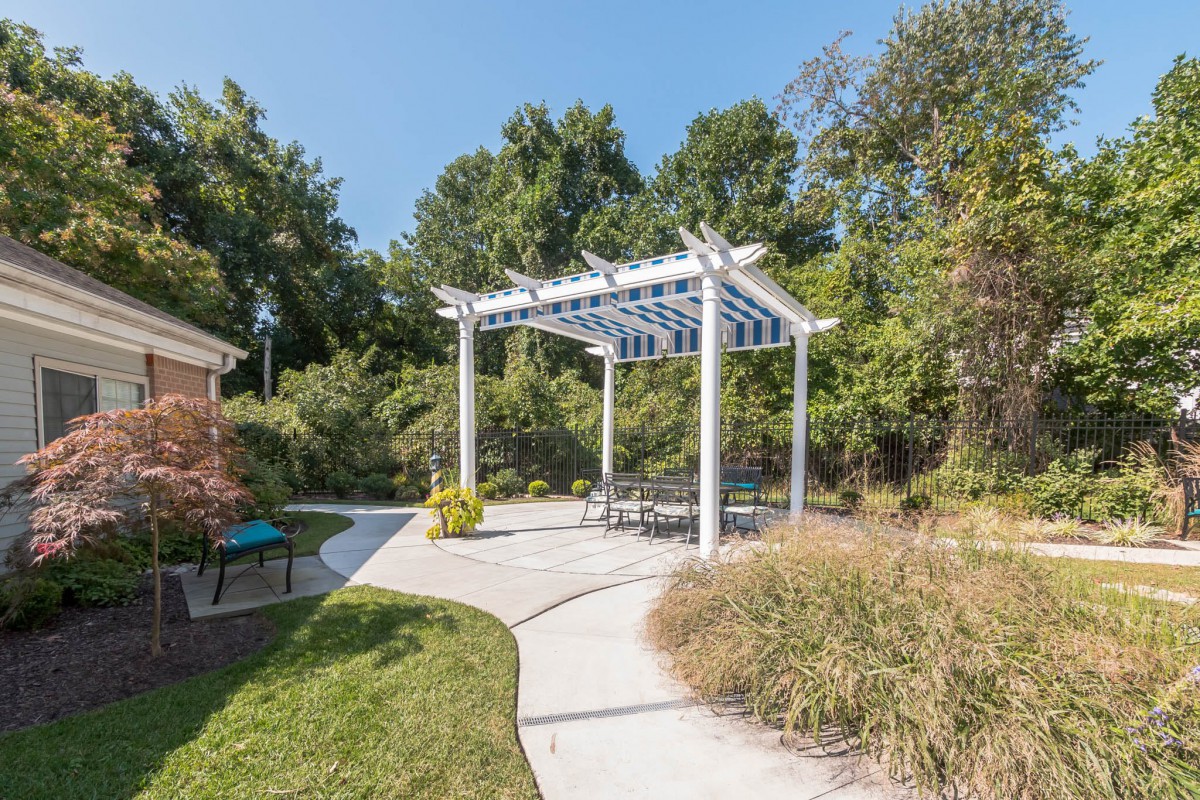 A peaceful garden setting featuring a white pergola with seating, surrounded by lush greenery and a winding pathway.