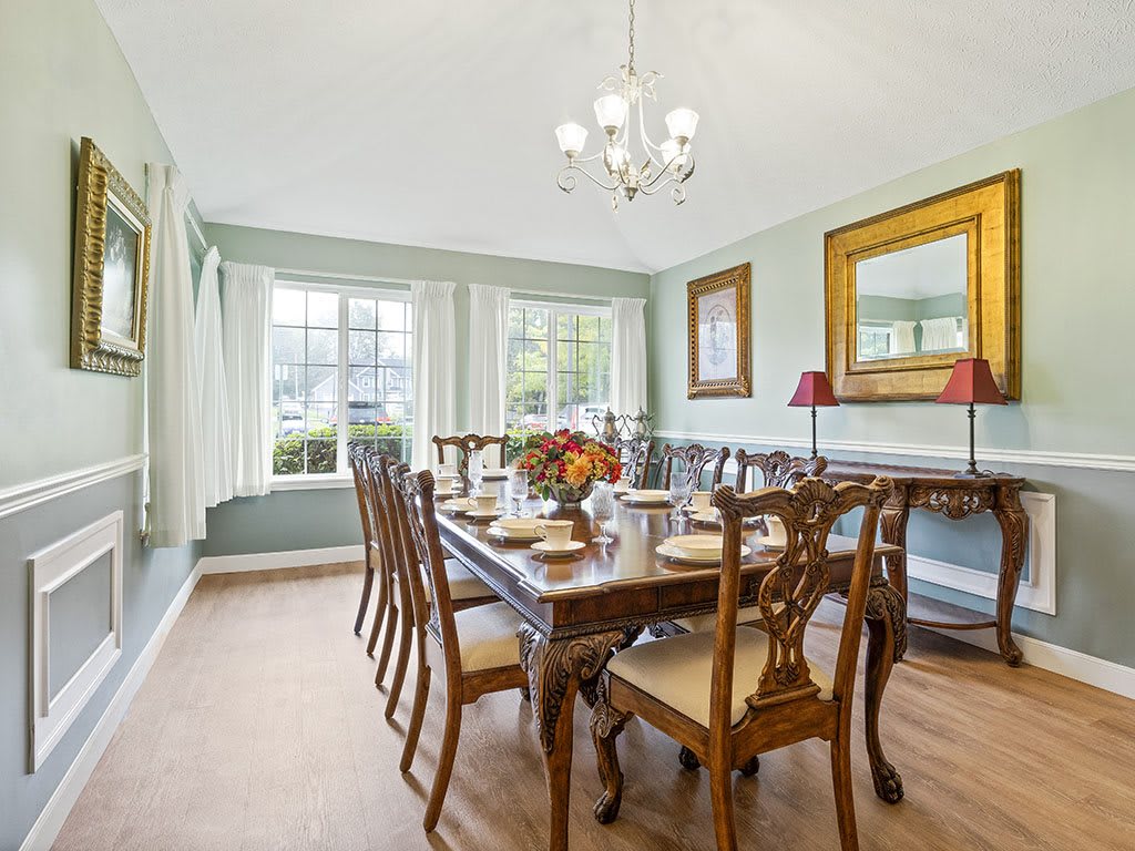 A spacious dining room with a large table set for a meal, surrounded by elegant chairs and illuminated by a chandelier.