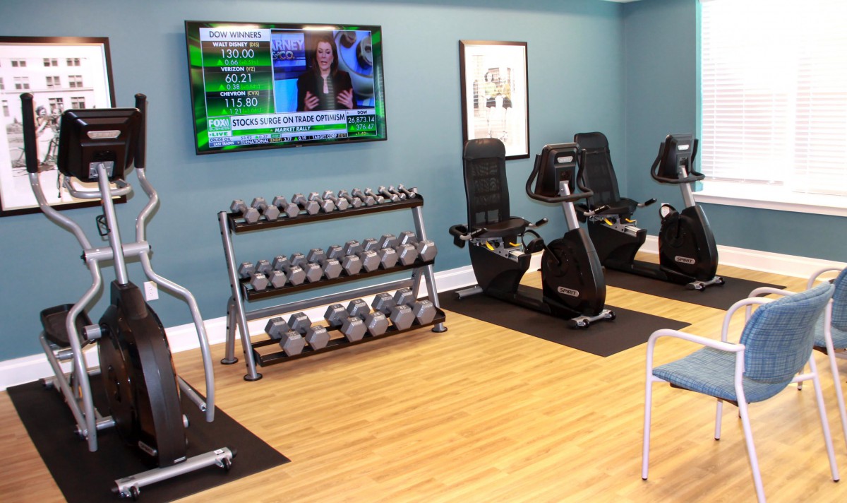 A modern gym setup with dumbbells, exercise bikes, and a television on the wall.