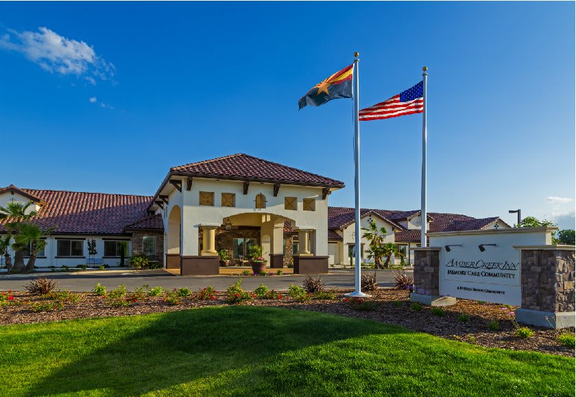 A building with a prominent entrance, surrounded by a well-kept lawn, with two flags flying under clear blue skies.