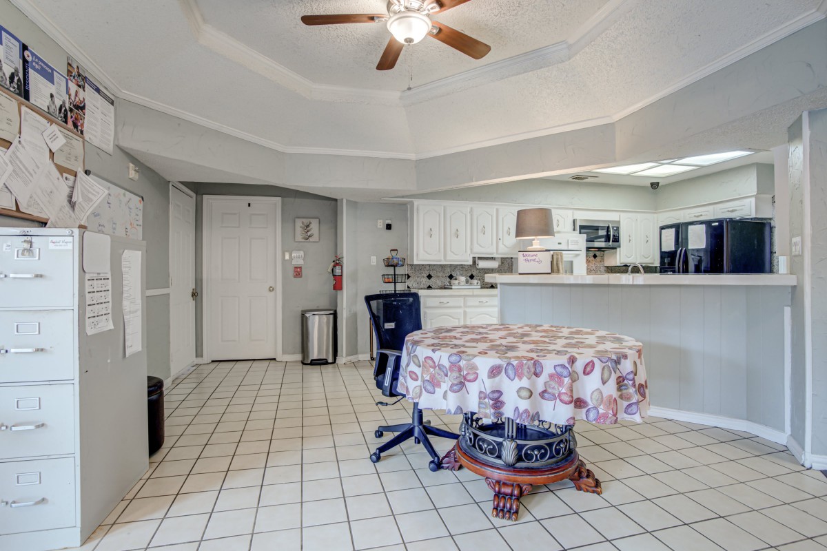A spacious kitchen with a tiled floor, featuring a round table, chairs, and a ceiling fan overhead.
