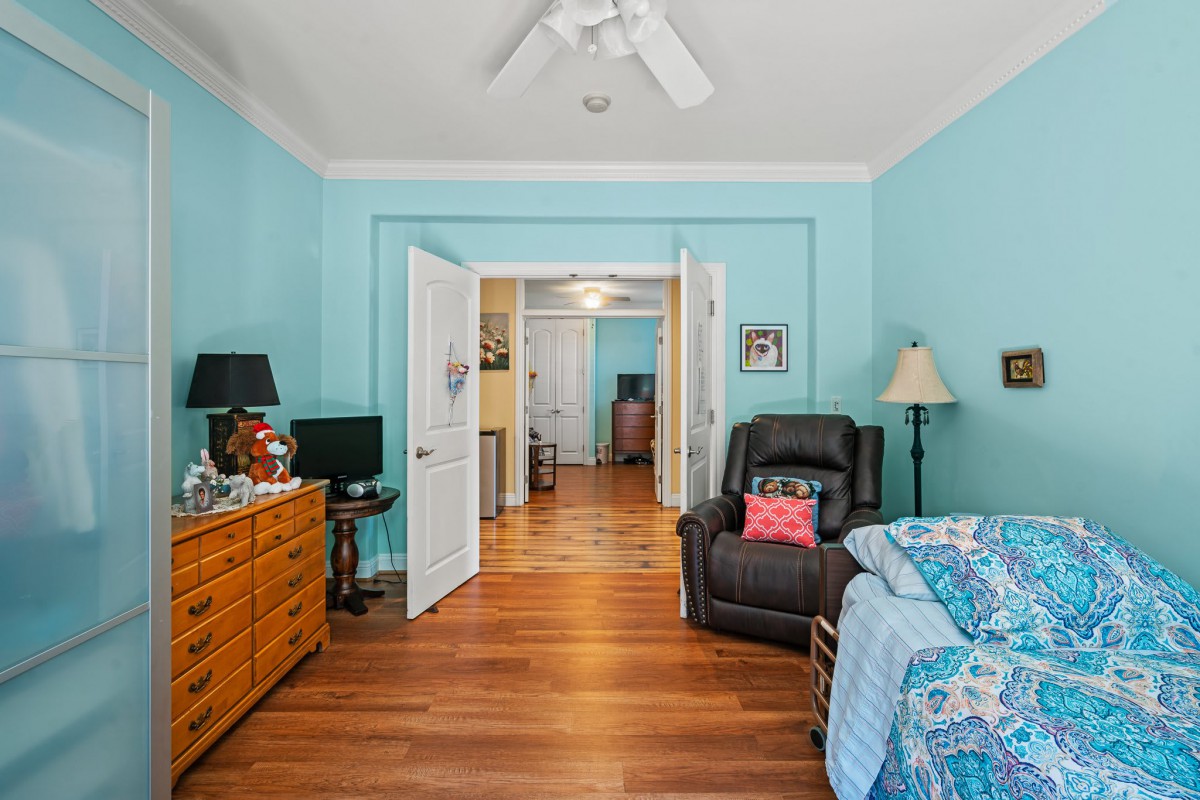 A cozy bedroom with turquoise walls and wood flooring, featuring a ceiling fan, armchair, dresser, and a lamp.
