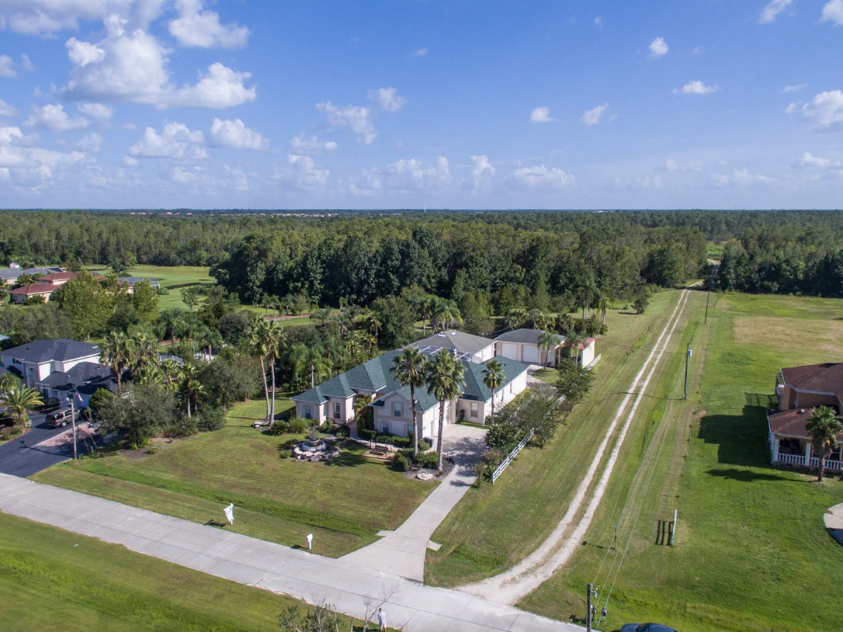 Aerial view of a large house in a rural setting surrounded by open fields and trees.