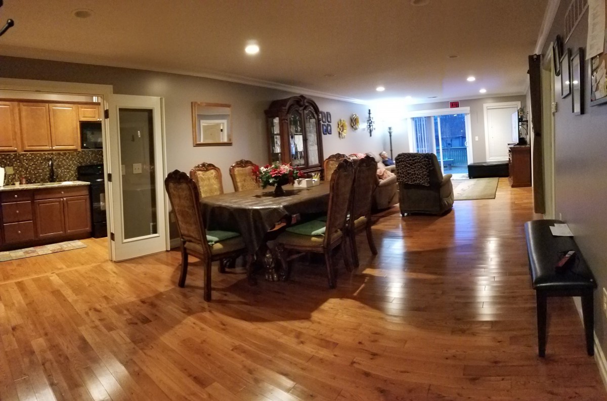 A spacious dining room with hardwood flooring, featuring a long table and several chairs.