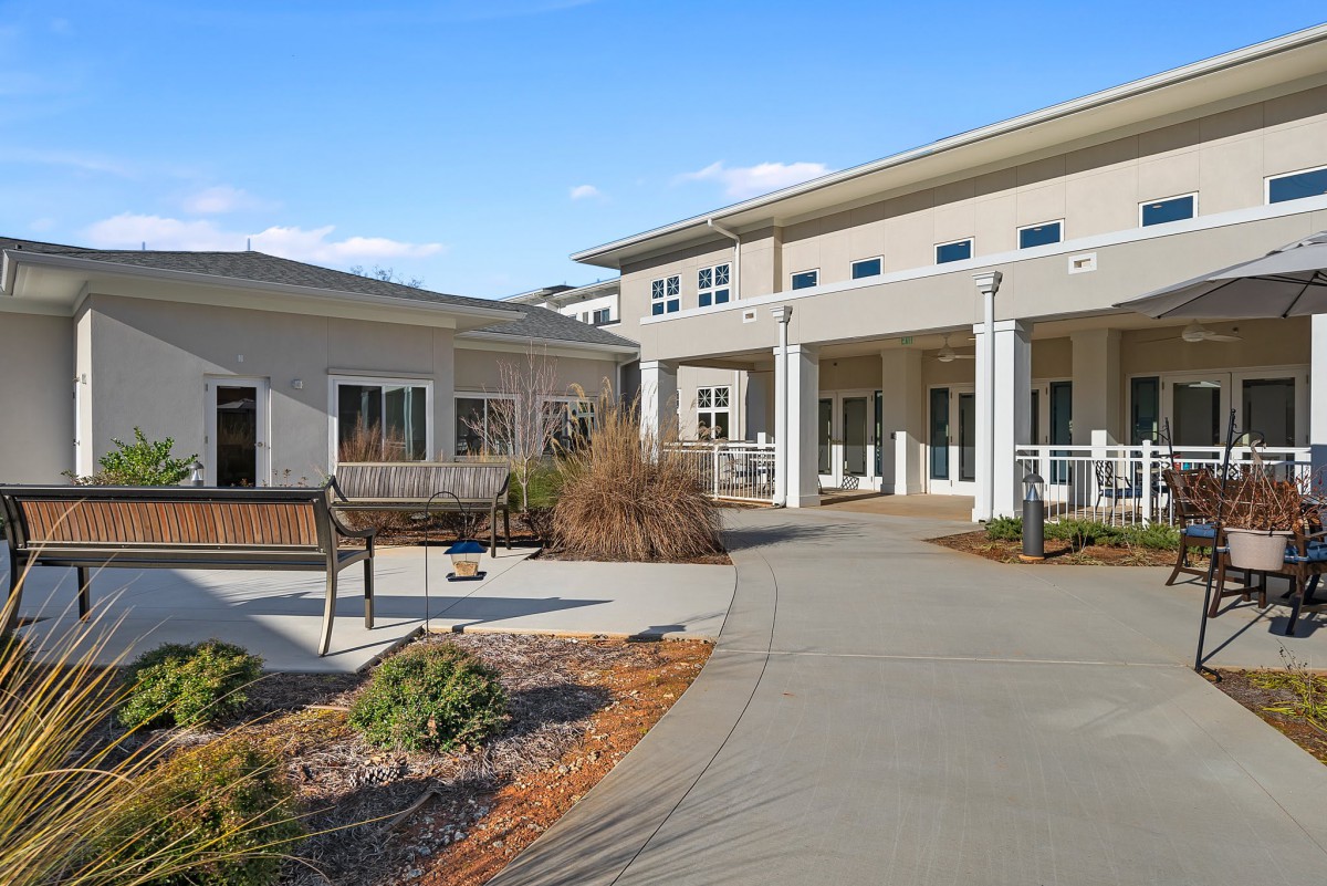 A modern building with a wide pathway and landscaped surroundings under a clear blue sky.