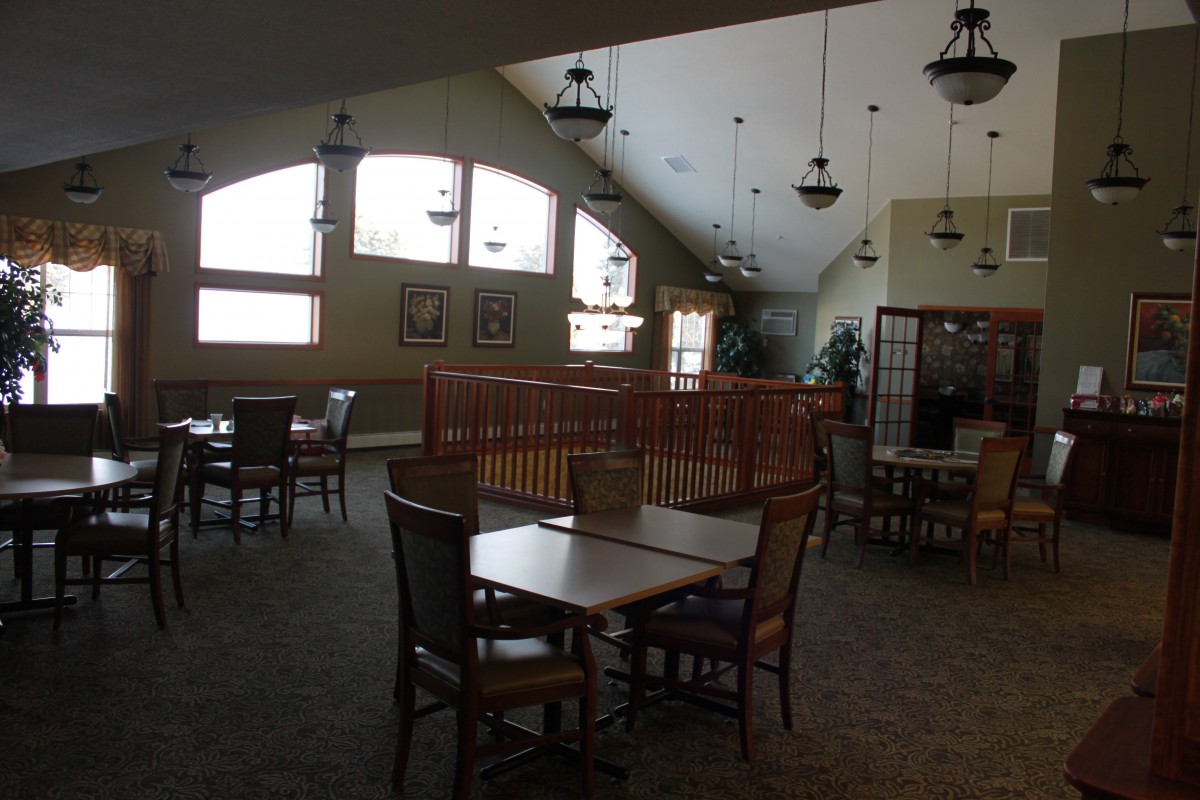 A spacious dining area with tables and chairs, featuring large windows and decorative lighting.