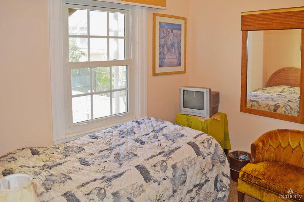 A cozy bedroom with a small TV, framed artwork, and a window letting in natural light.