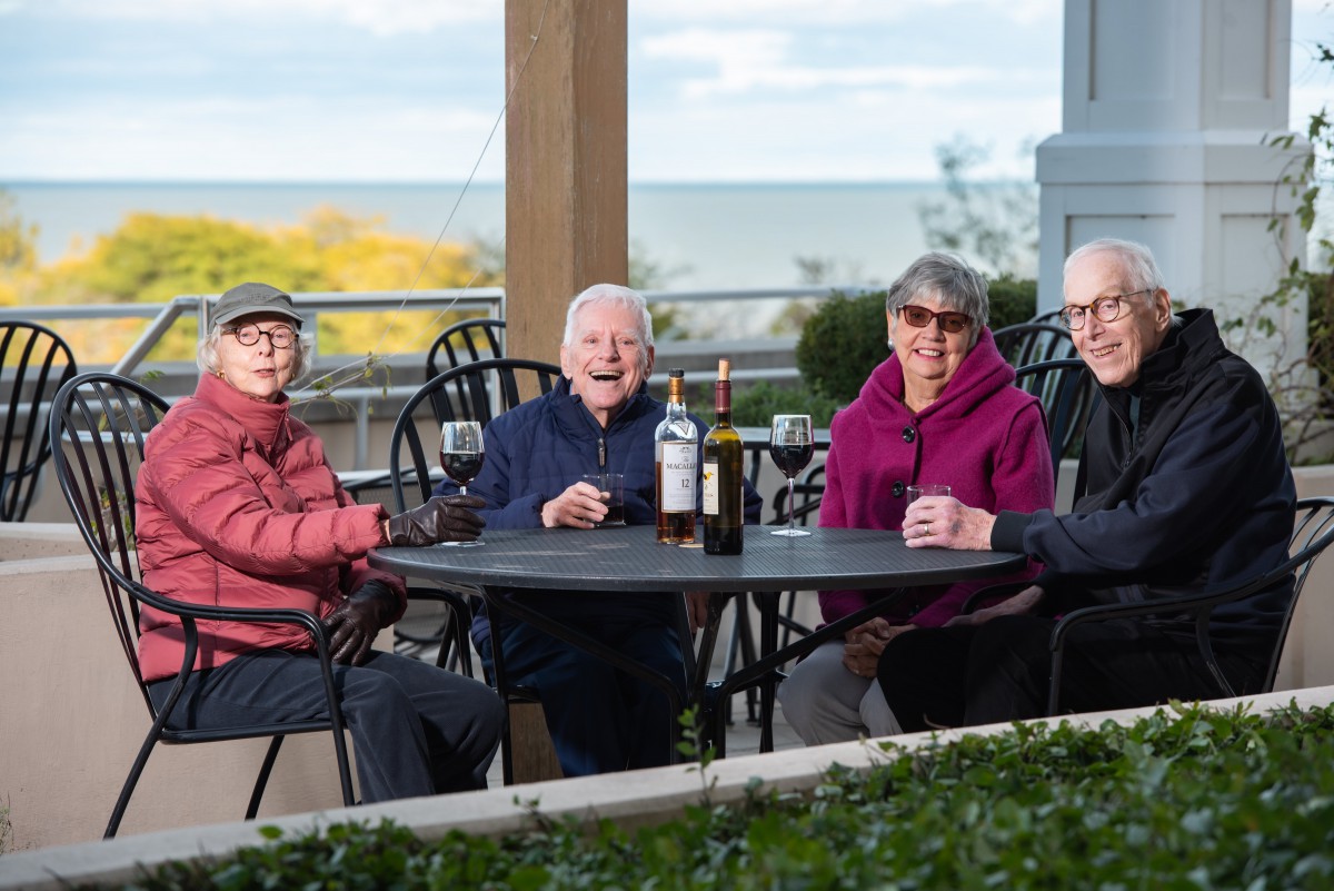 A group of elderly people enjoying drinks and socializing at an outdoor table.