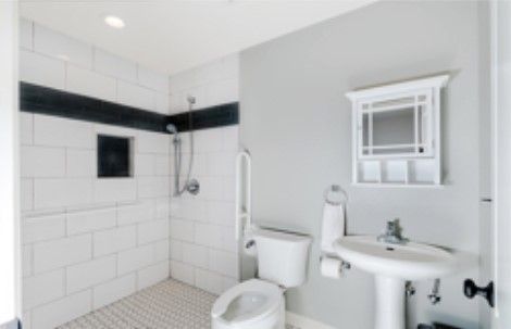 A modern bathroom with a walk-in shower, toilet, and pedestal sink.