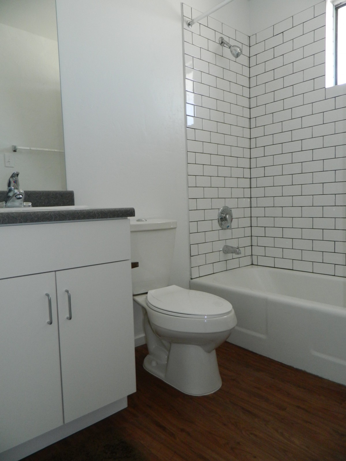 A modern bathroom with white subway tiles, featuring a bathtub, toilet, and sink.