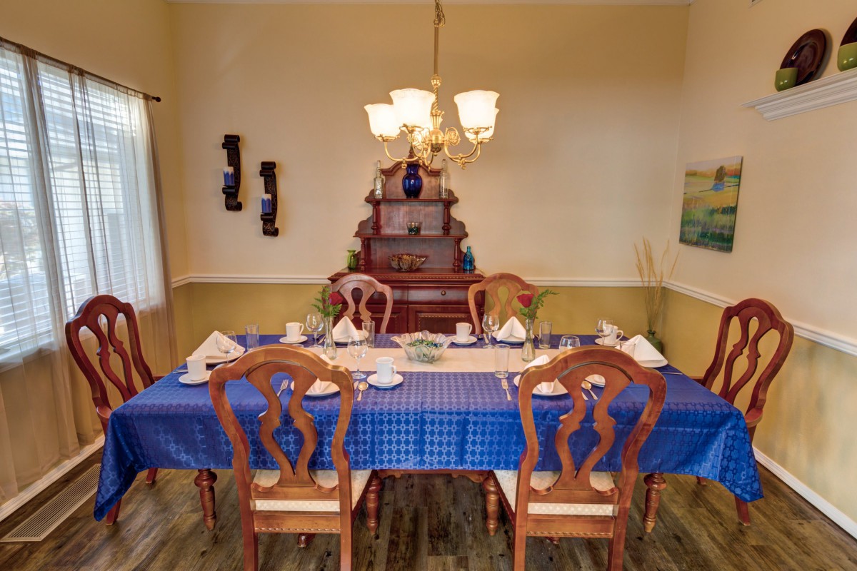 A dining room setup with a blue tablecloth, wooden chairs, and a chandelier overhead.