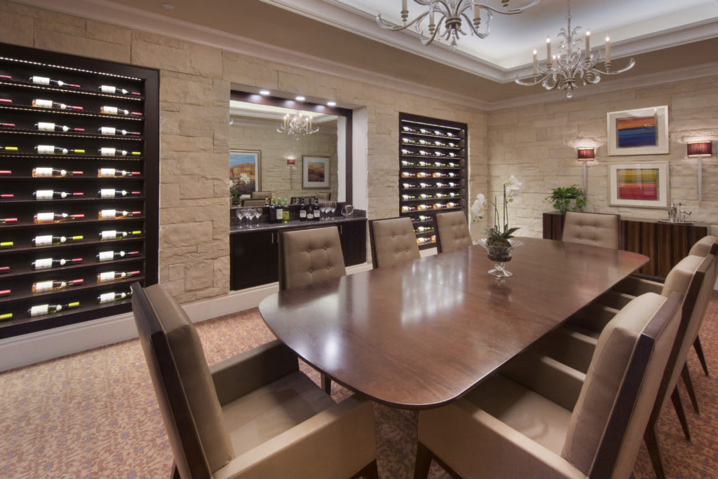 A luxurious dining room with a large wooden table, surrounded by elegant chairs and flanked by wine storage racks.