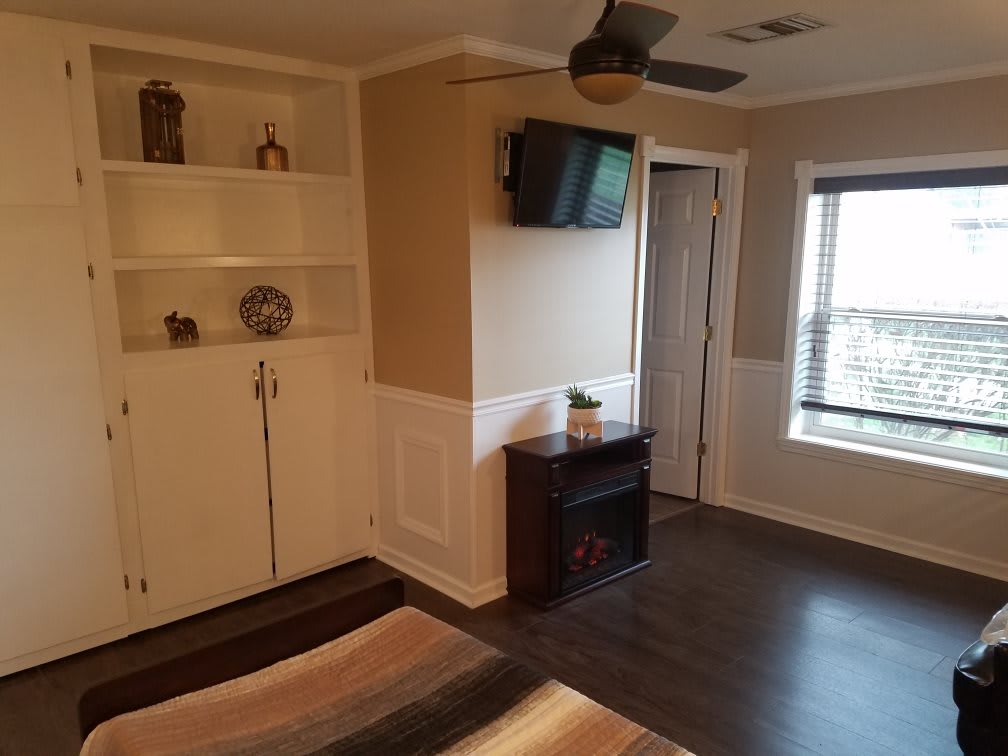 A cozy bedroom with a wall-mounted TV, built-in shelves, and a large window.