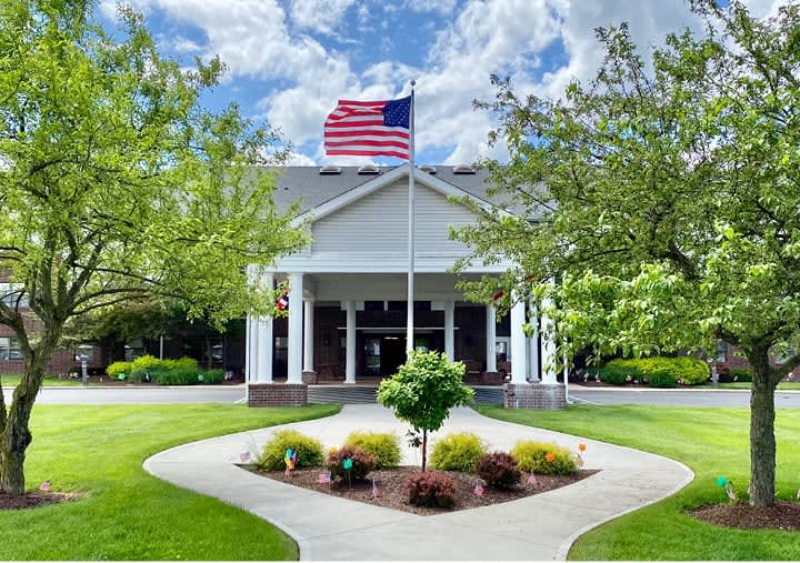 A building entrance with an American flag flying above, surrounded by well-maintained landscaping under a partly cloudy sky.