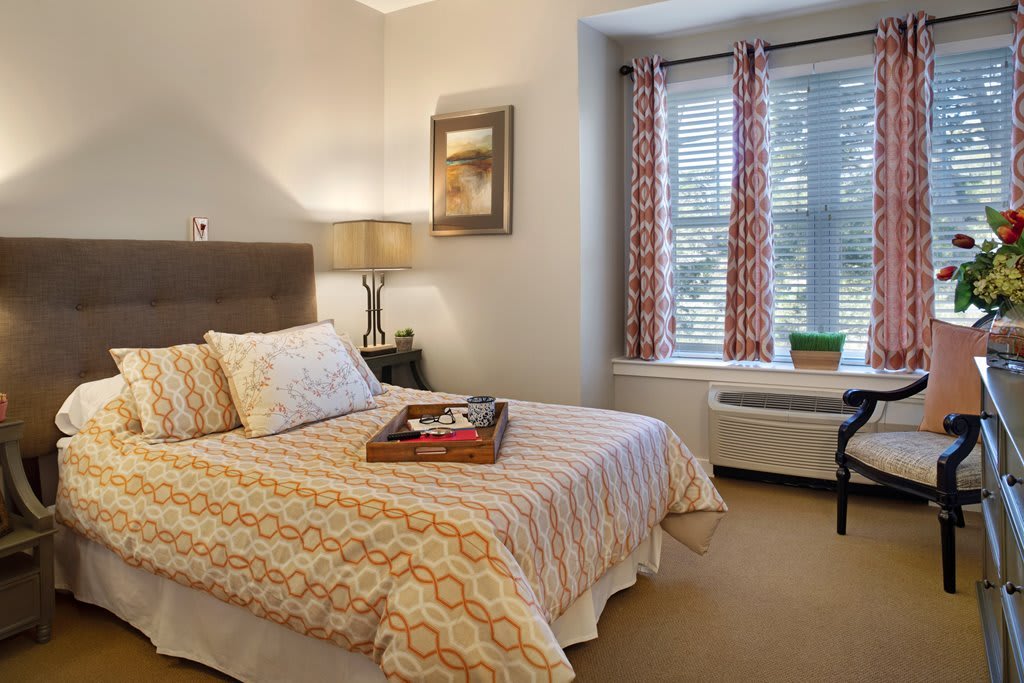 A cozy bedroom with a neatly made bed, decorative pillows, and natural light streaming through the window.