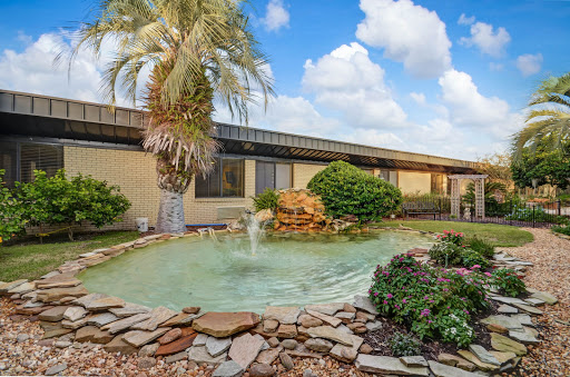 A serene garden with a fountain, surrounded by lush greenery and a beautiful sky.