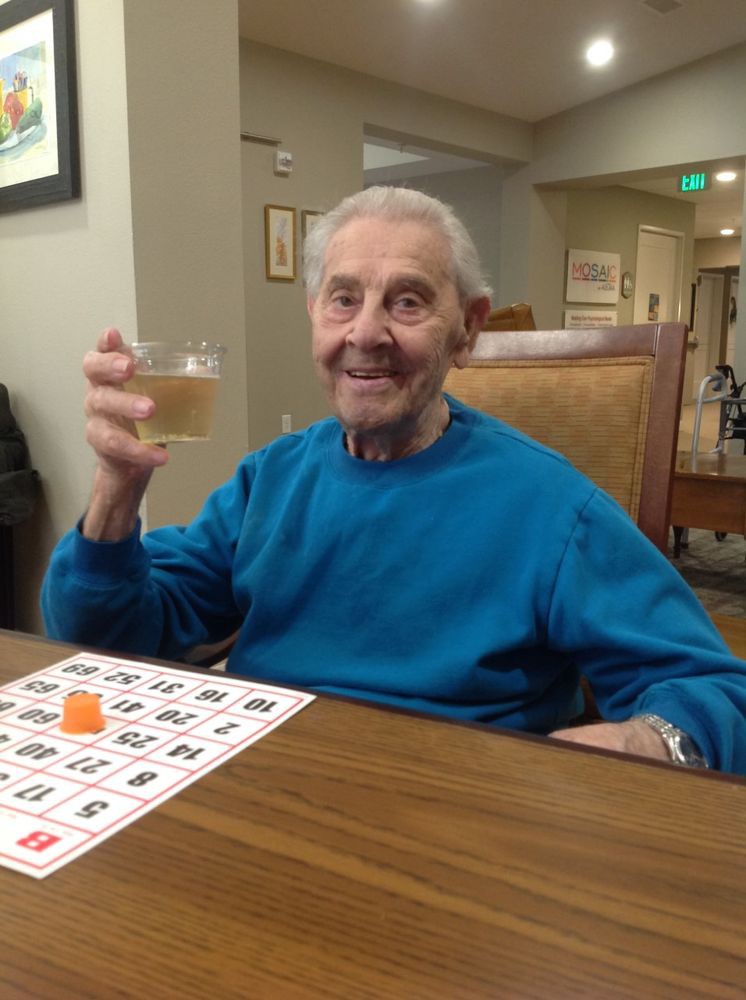 An elderly man enjoying a game of bingo while holding a drink and smiling indoors.
