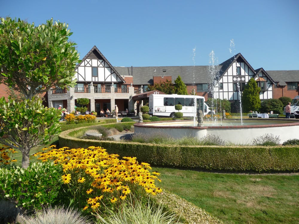 A scenic view of a garden with a fountain and a Tudor-style building in the background on a sunny day.