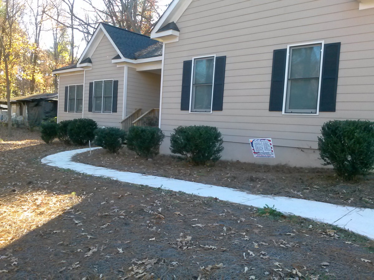 A beige house with a front walkway and neatly trimmed shrubs.