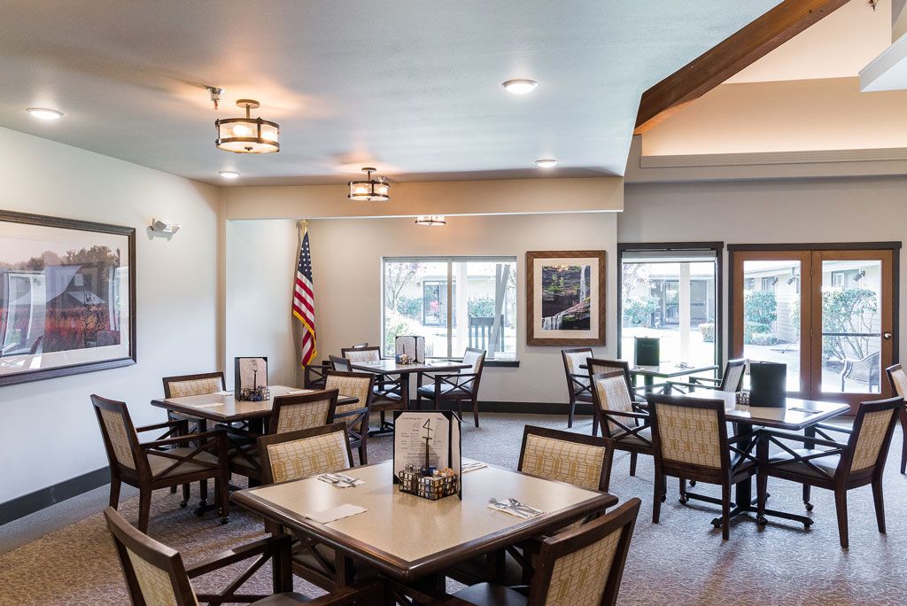 A modern dining room with multiple tables and chairs, featuring large windows and elegant lighting.
