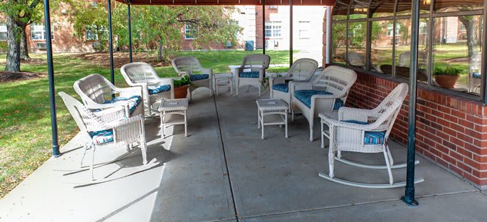 A cozy outdoor seating area with wicker furniture and blue cushions, situated under a covered patio.