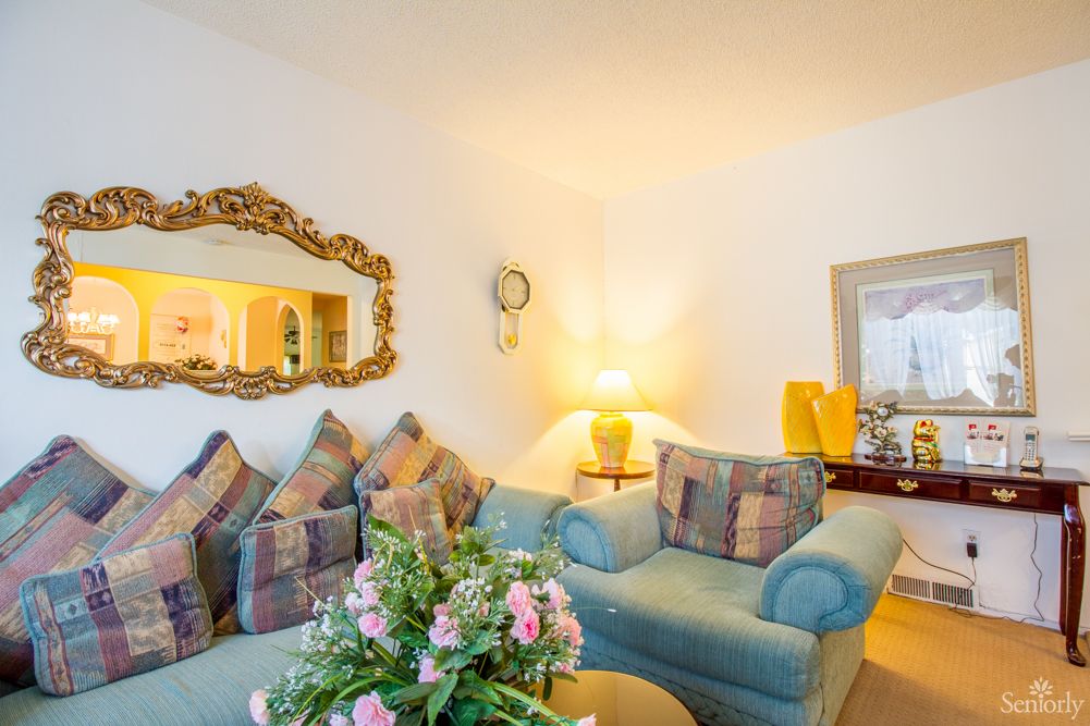 A cozy living room featuring a comfortable sofa adorned with patterned cushions, a decorative mirror, and a soft-lit lamp on the side table.