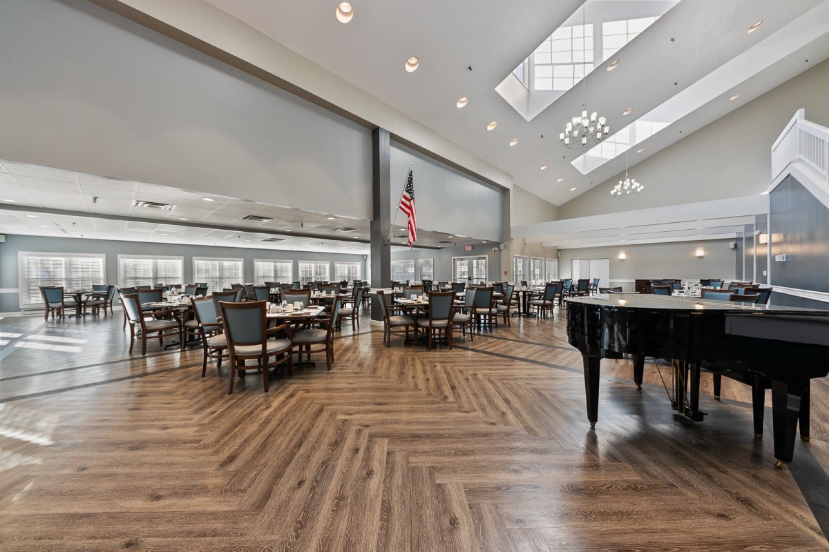 A spacious dining area with elegant furniture and a grand piano, illuminated by natural light from skylights and large windows.