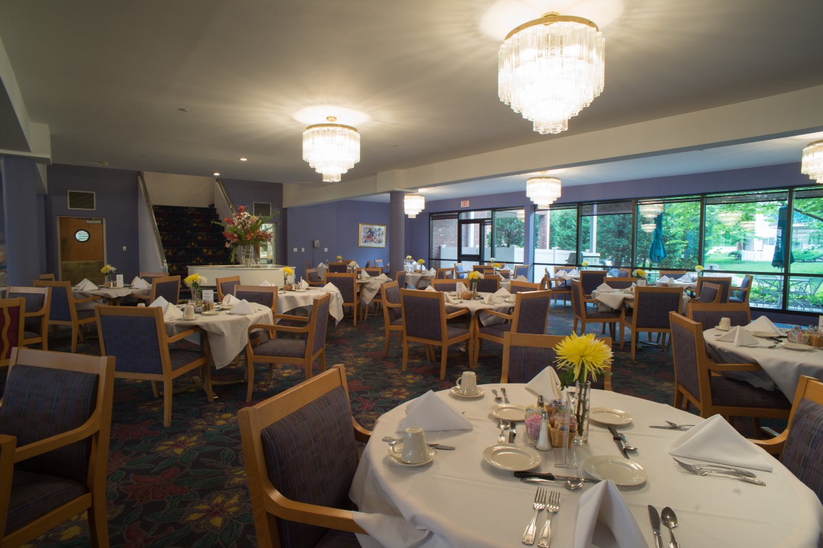 A spacious and elegantly decorated restaurant dining room with empty tables and chairs under chandeliers.
