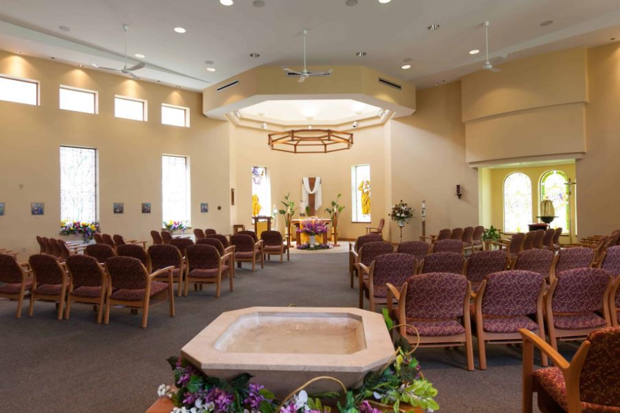 Interior view of a church with seating, an altar, and a baptismal font adorned with flowers.