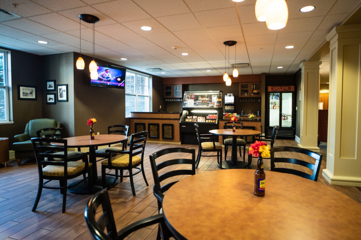 A cozy and modern cafe interior with tables and chairs arranged neatly under warm lighting.