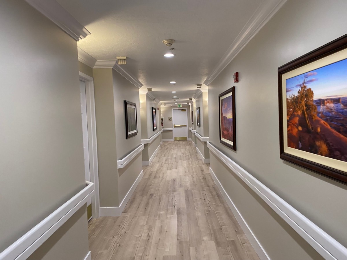 A well-lit hallway with paintings on the walls and wooden flooring.