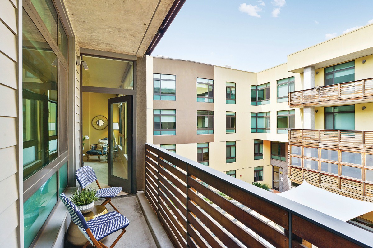 A modern apartment balcony with outdoor seating and a view of adjacent buildings.