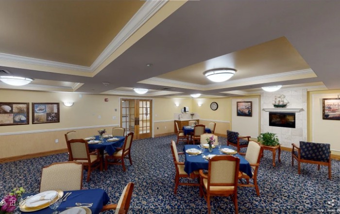A cozy dining room with neatly arranged tables and chairs, featuring blue tablecloths and warm lighting.