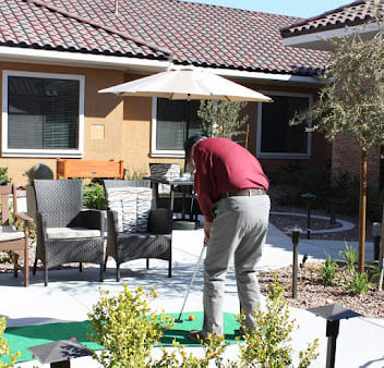 A person playing golf on a putting green in a garden setting.