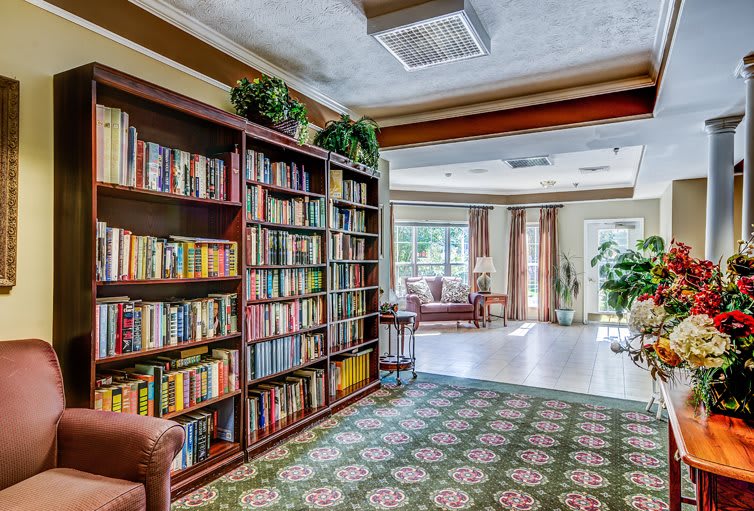 A cozy library corner with a large bookshelf filled with books, comfortable seating, and natural light streaming through the windows.