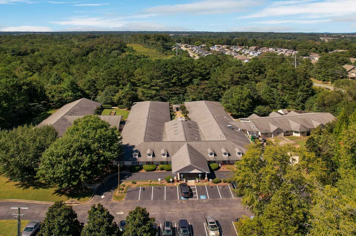Aerial view of a building surrounded by trees with a parking lot in the foreground.