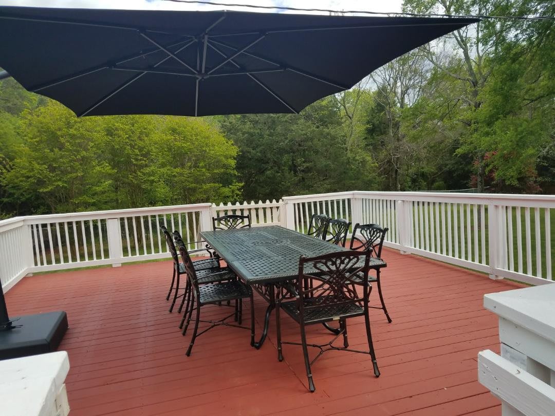 A peaceful outdoor patio with a table, chairs, and an umbrella overlooking lush greenery.