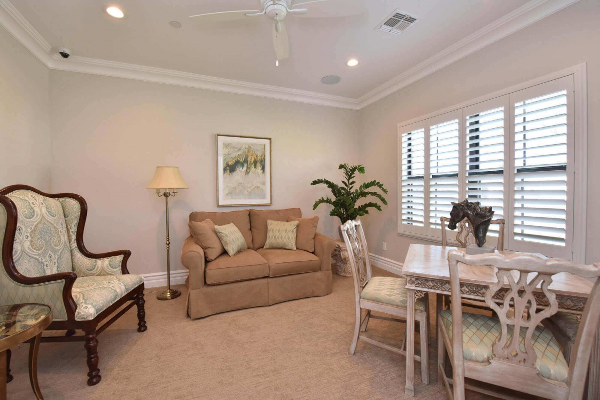 A cozy living room featuring a sofa, dining table with chairs, a tall lamp, and an indoor plant near the window.
