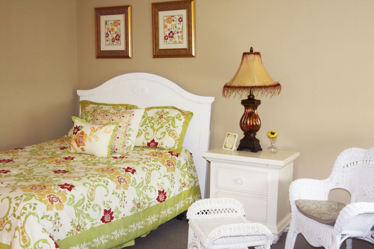 A cozy bedroom with floral bedding, a white nightstand, and a decorative lamp.