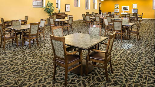A spacious dining area featuring wooden tables and chairs, accented by a patterned carpet.