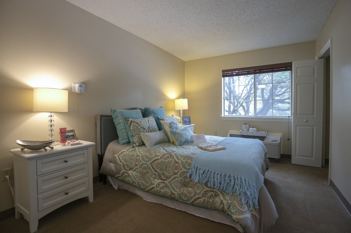 A cozy bedroom with a neatly made bed, soft lighting, and a window view.