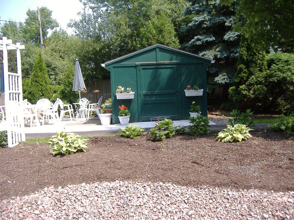 A landscaped garden with a green shed, patio seating, and various plants.