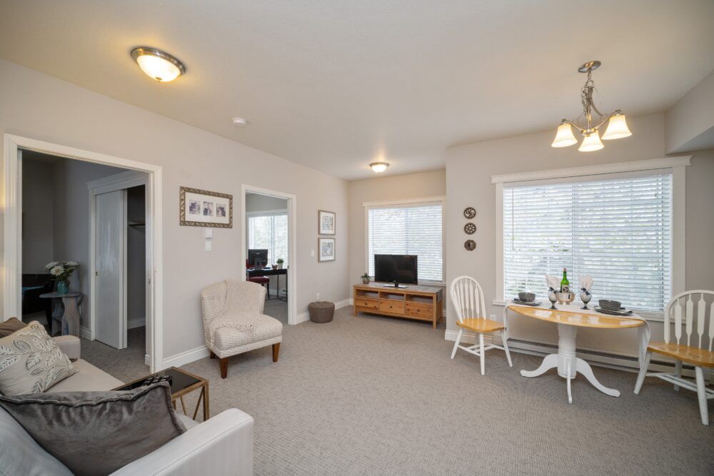A cozy living room with neutral tones, featuring comfortable furniture and a small dining area by the window.
