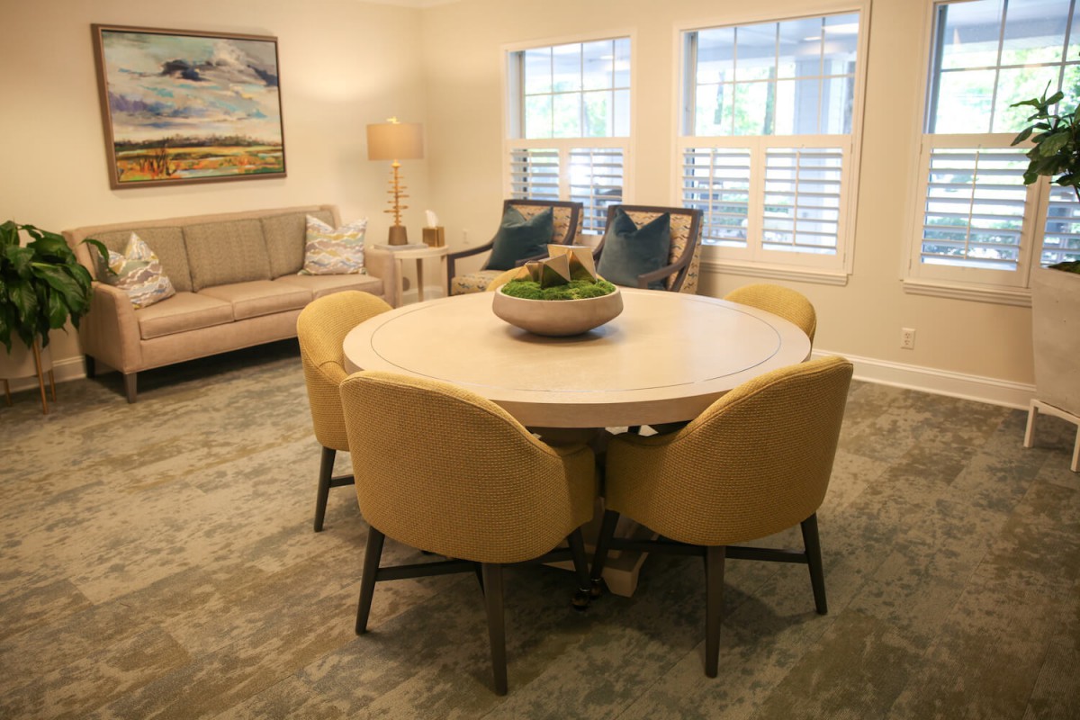 A cozy living room with a round table surrounded by yellow chairs, a sofa, and decorative elements.