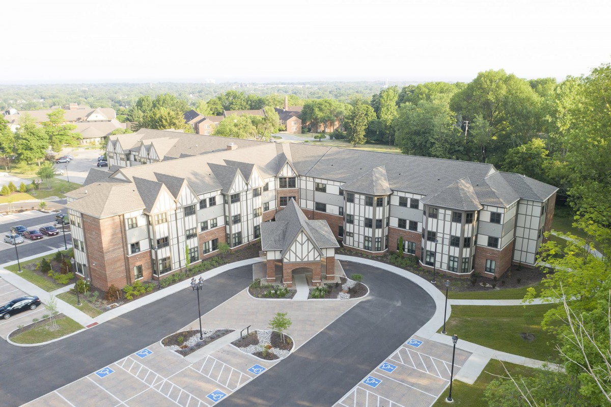 Aerial view of a large residential building with a parking lot and surrounding greenery.