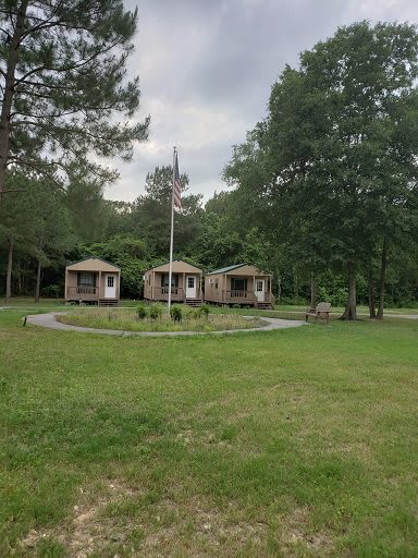 Three small cabins surrounded by trees and grass under an overcast sky.