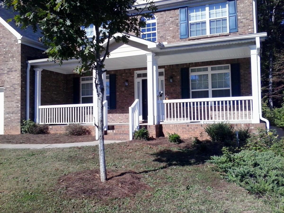 A suburban house with a brick exterior and a front porch, featuring a small tree and lawn.